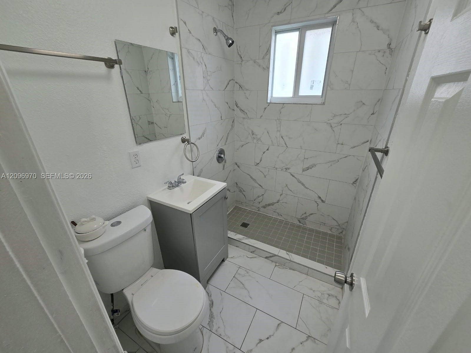 535 NW 7th Street, #12, Miami, Miami, FL 33136 Bathroom featuring floor-to-ceiling large-format tile with veining, grey vanity cabinet, white sink basin, and glass-paneled walk-in shower