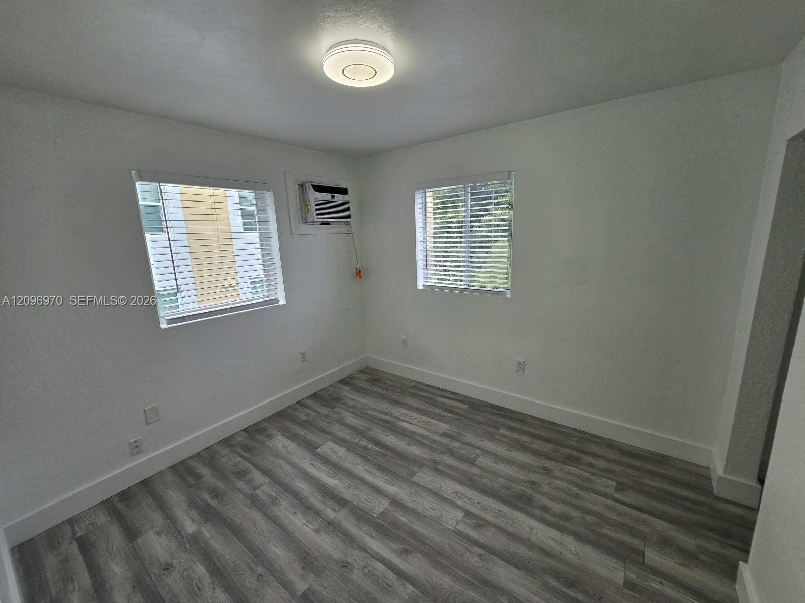 535 NW 7th Street, #12, Miami, Miami, FL 33136 Neutral-toned wood-finish flooring, two windows with horizontal blinds, flush-mount ceiling light fixture, and wall-mounted air conditioning unit