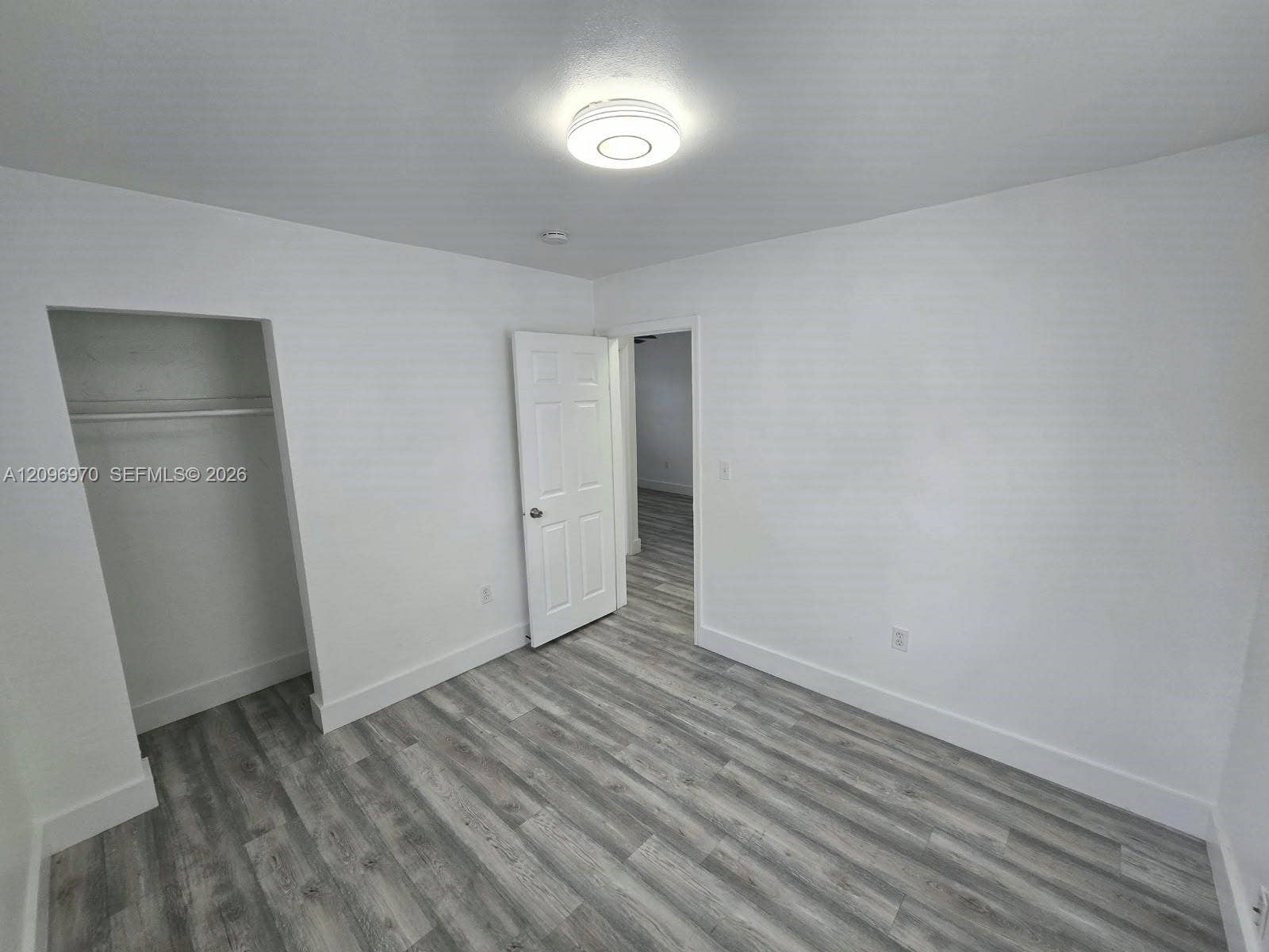 535 NW 7th Street, #12, Miami, Miami, FL 33136 Neutral interior room featuring wood-finish flooring, a six-panel interior door, a built-in closet with overhead shelving, and a circular flush-mount ceiling light fixture