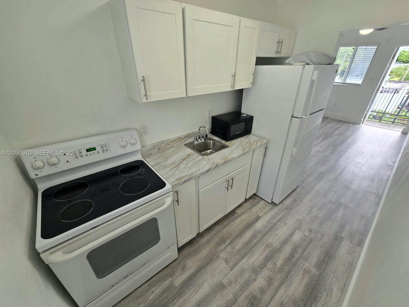 535 NW 7th Street, #12, Miami, Miami, FL 33136 Kitchen featuring white shaker-style cabinetry, stone-pattern laminate countertops, wood-finish flooring, and a full-size white electric range