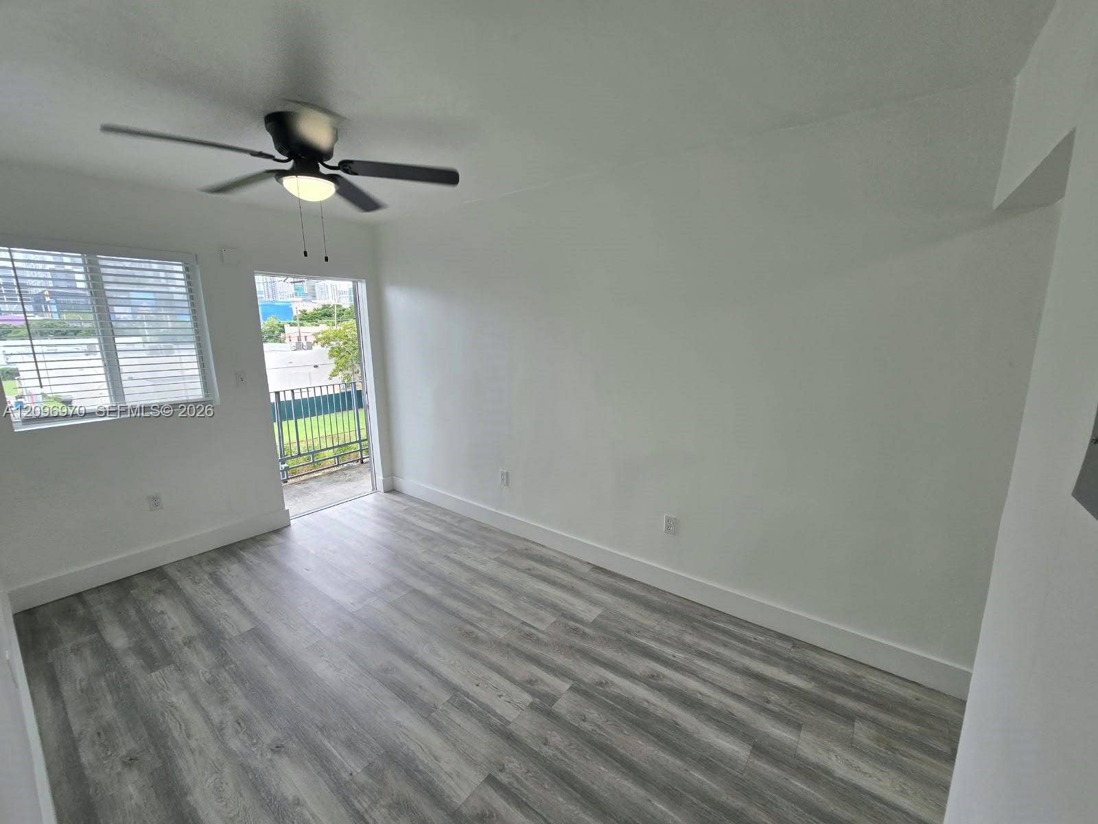 535 NW 7th Street, #12, Miami, Miami, FL 33136 Interior space featuring wood-finish flooring, a multi-blade ceiling fan with integrated light fixture, a window with horizontal blinds, and access to a balcony with metal railing