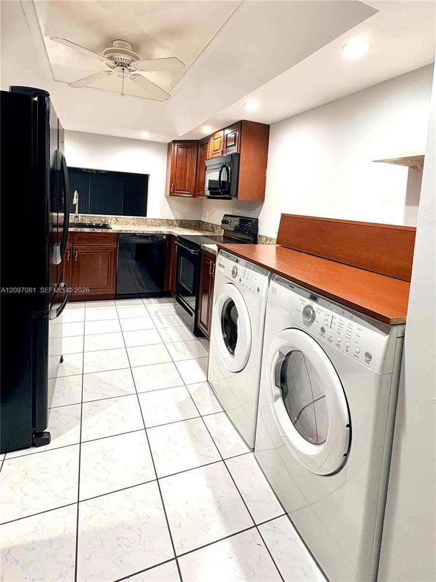 3271 Coral Springs Drive, #2, Coral Springs, Coral Springs, FL 33065 Kitchen featuring wood cabinetry, stone-finish countertops, tile flooring, built-in black appliances, and laundry area with an integrated wood-surface folding counter