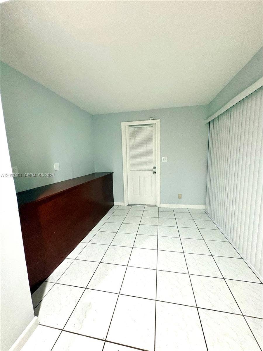 3271 Coral Springs Drive, #2, Coral Springs, Coral Springs, FL 33065 Room featuring light-colored tile flooring, built-in custom cabinetry with a wood-tone finish, a single-panel exterior door, and large vertical blinds