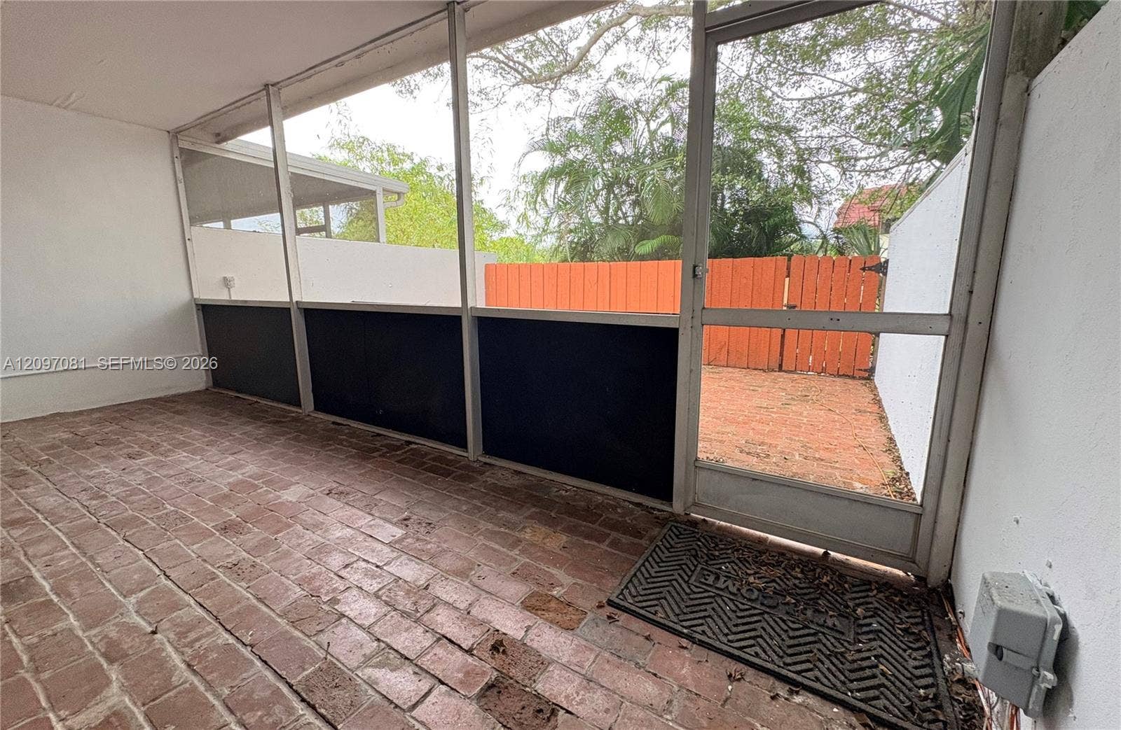3271 Coral Springs Drive, #2, Coral Springs, Coral Springs, FL 33065 Screened-in patio featuring brick flooring, white wall finishes, and a swinging aluminum-frame door opening to a private outdoor space with a privacy fence