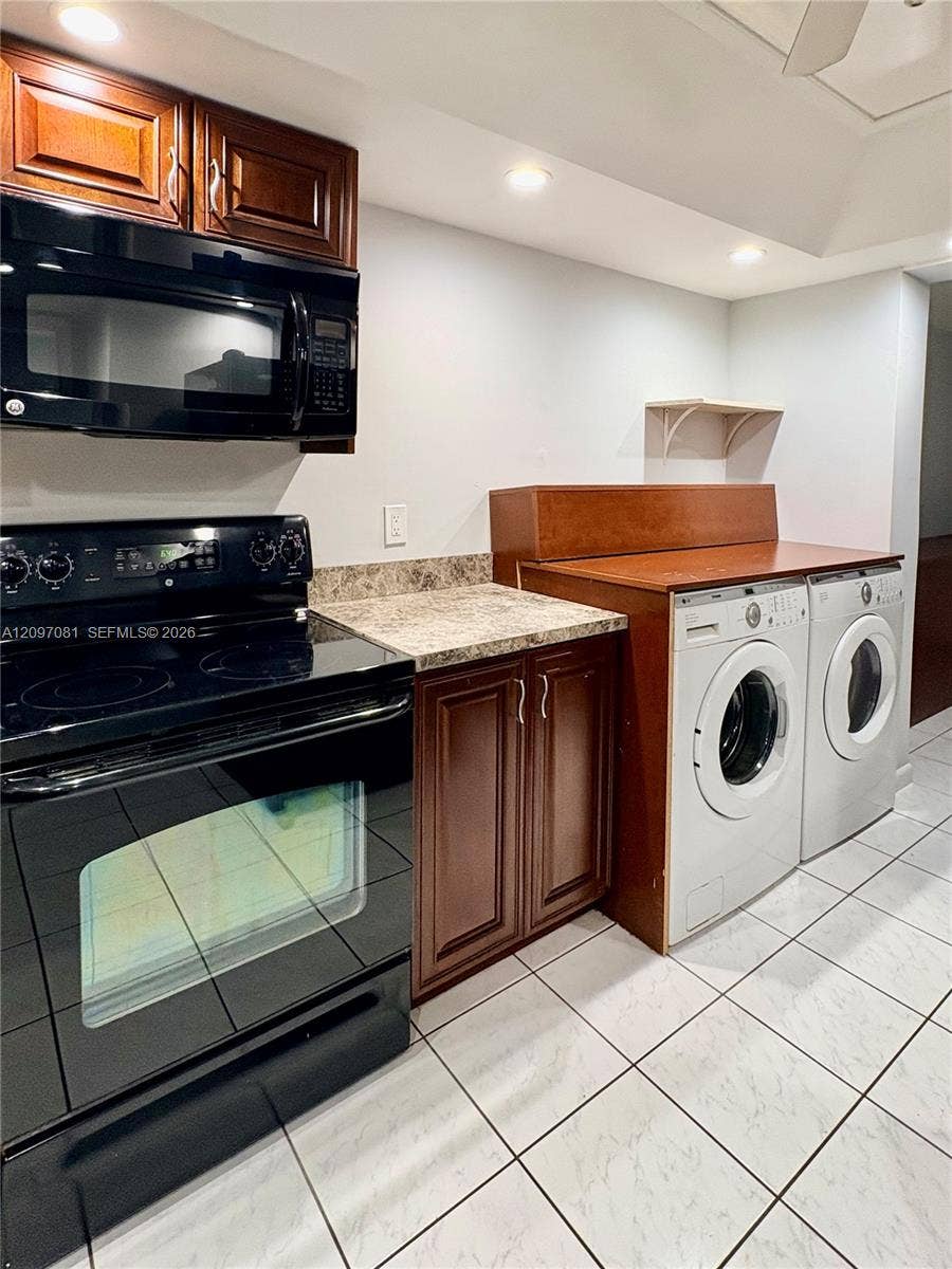 3271 Coral Springs Drive, #2, Coral Springs, Coral Springs, FL 33065 Custom cabinetry with rich wood finish, stone-patterned countertops, black electric range with over-the-range microwave, and ceramic tile flooring