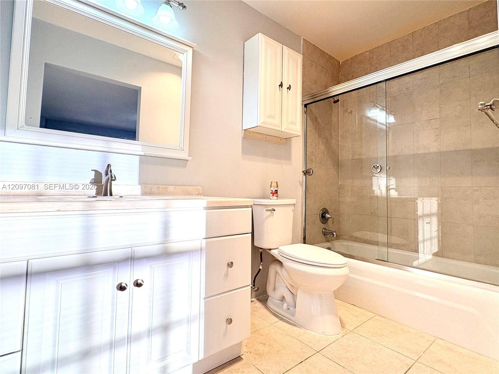 3271 Coral Springs Drive, #2, Coral Springs, Coral Springs, FL 33065 Bathroom featuring white shaker-style cabinetry, framed vanity mirror, wall-mounted storage cabinet, tile-surround tub with sliding glass doors, and light-toned floor tile
