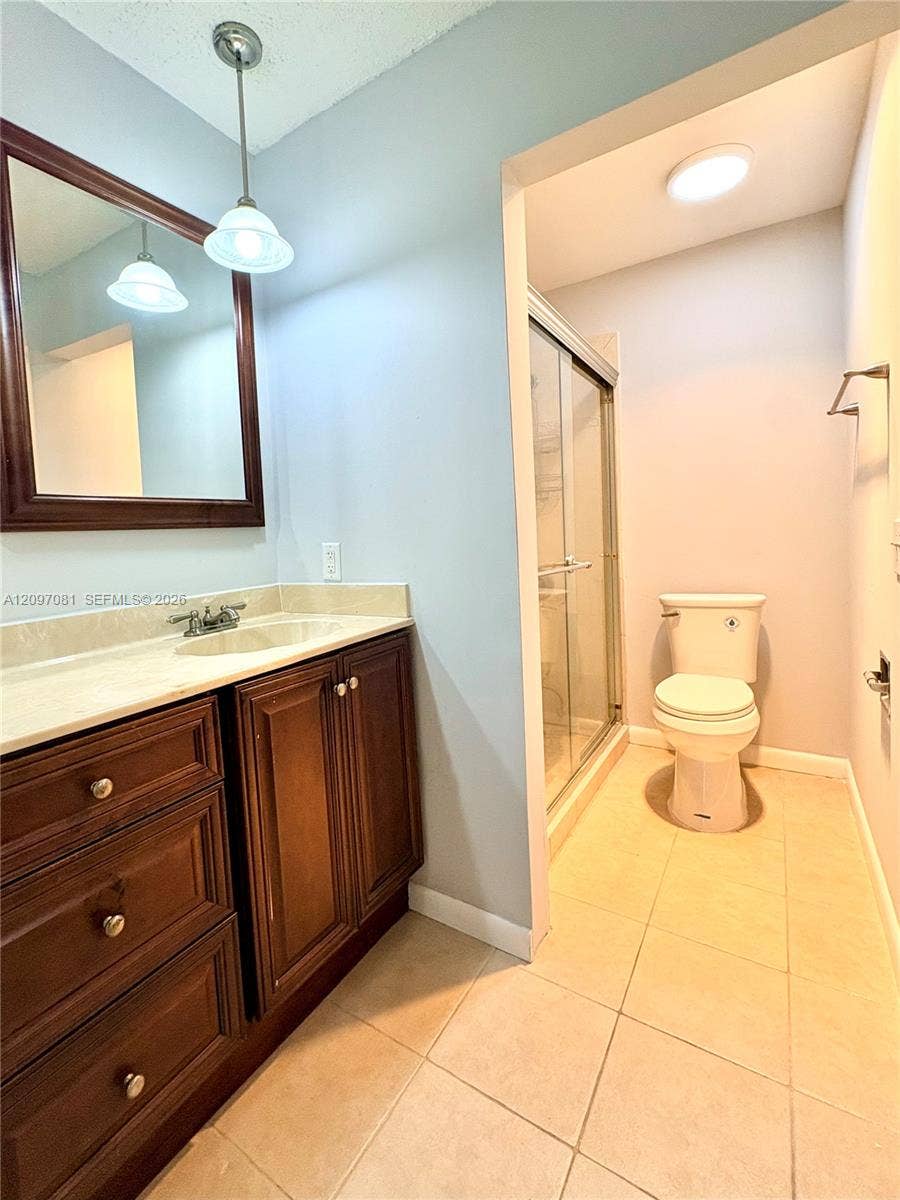 3271 Coral Springs Drive, #2, Coral Springs, Coral Springs, FL 33065 Bathroom vanity featuring wood cabinetry, stone-finish countertop, undermount sink, and wall-mounted pendant lighting, accompanied by a walk-in shower with a glass enclosure and a ceramic tile floor