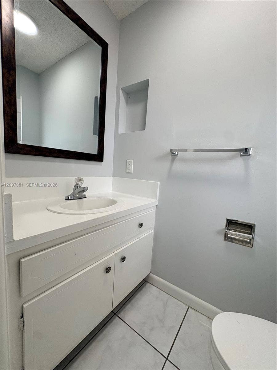 3271 Coral Springs Drive, #2, Coral Springs, Coral Springs, FL 33065 White vanity featuring an integrated basin and solid-surface countertop, paired with a dark-frame wall mirror, recessed wall niche, and ceramic tile flooring