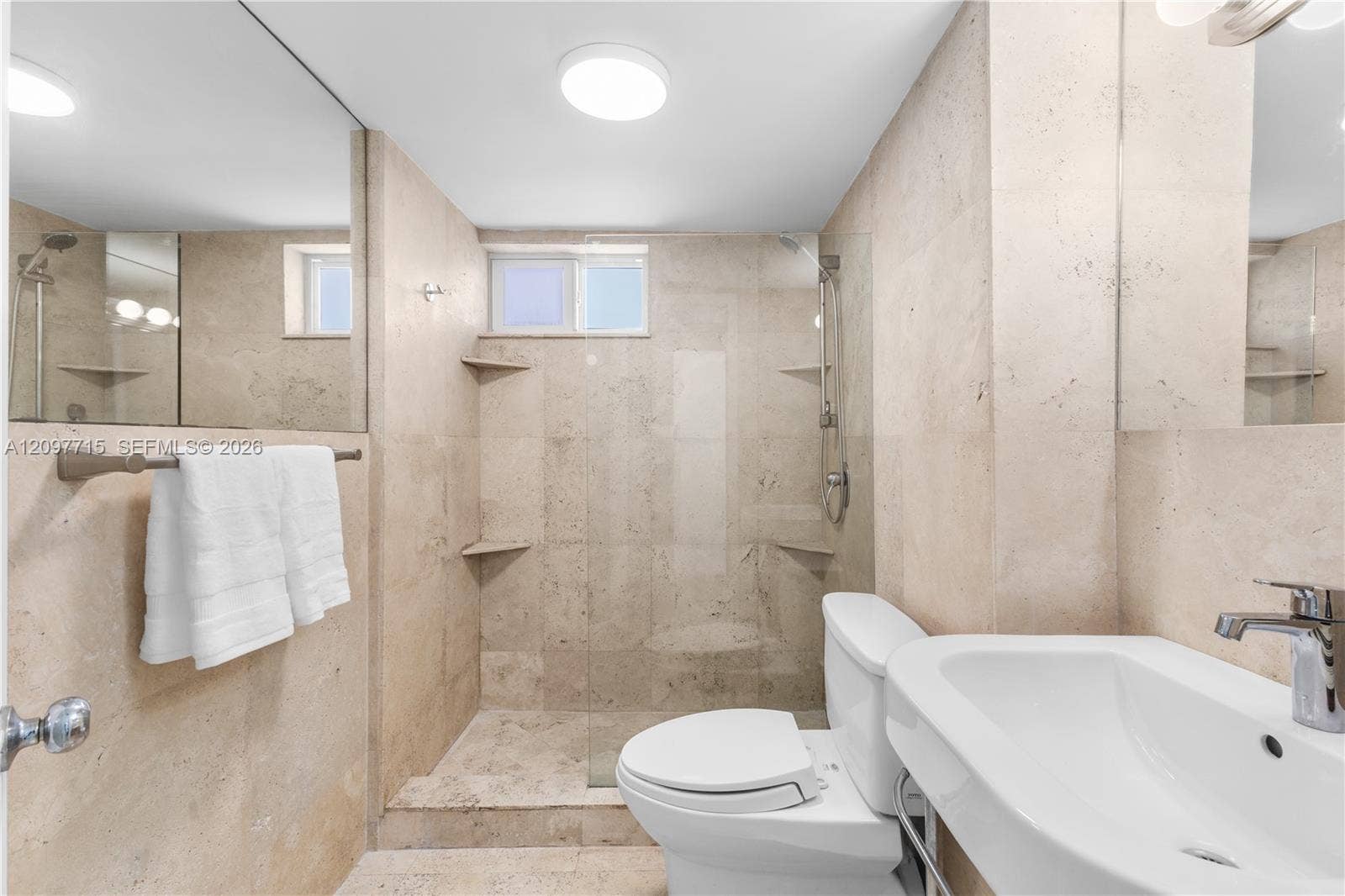 Full-height tiled walls, walk-in shower with built-in shelving, flush-mount lighting, and wall-mounted vanity sink