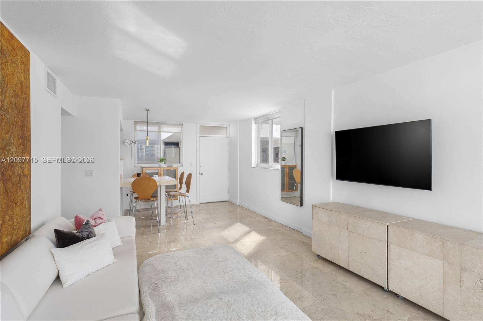 Open-concept living area featuring light-toned flooring, white walls, and a recessed wall-mounted media console