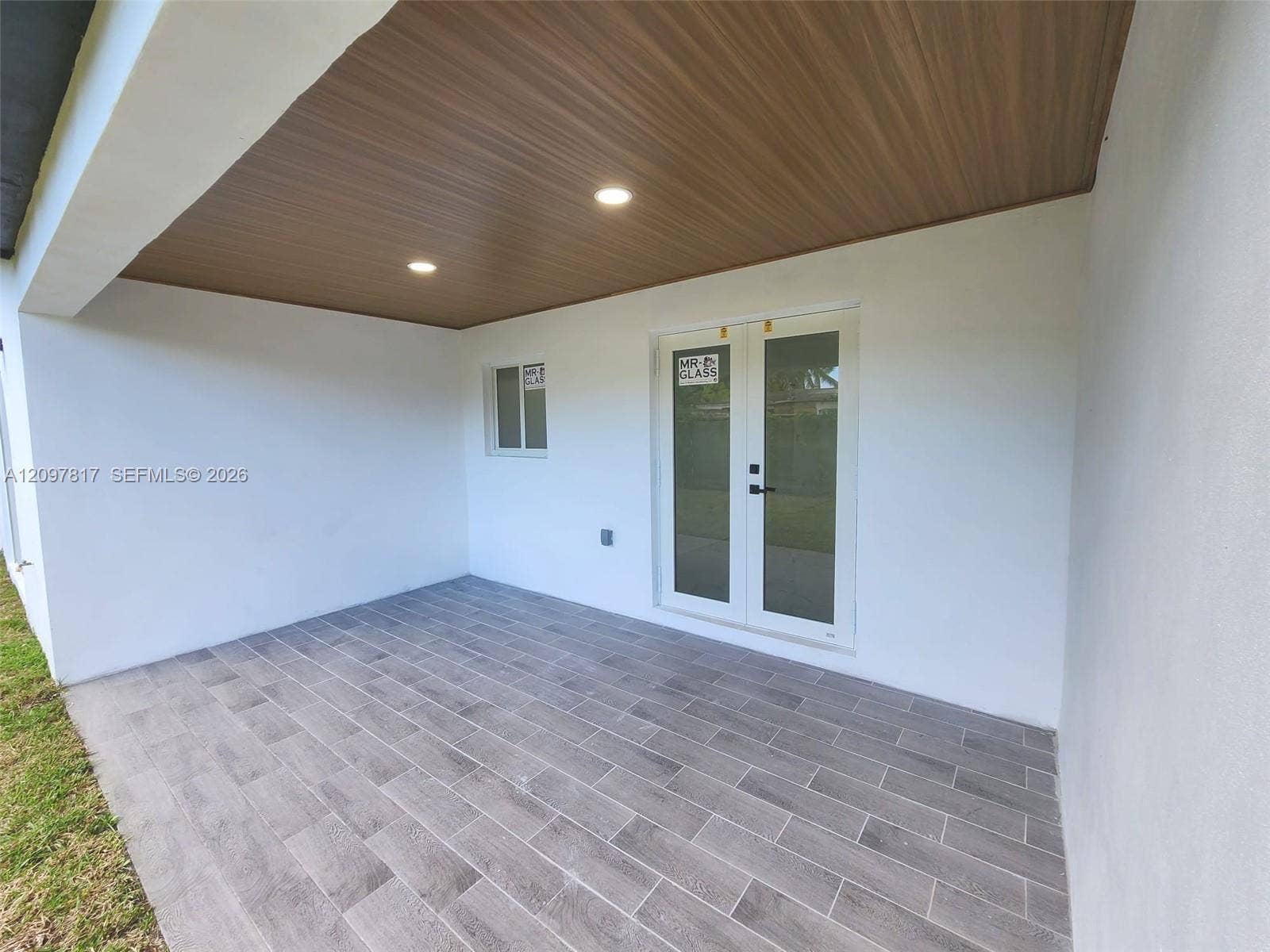 Covered patio featuring wood-finish ceiling paneling, recessed lighting, white exterior walls, and gray stone-finish tile flooring with double glass doors