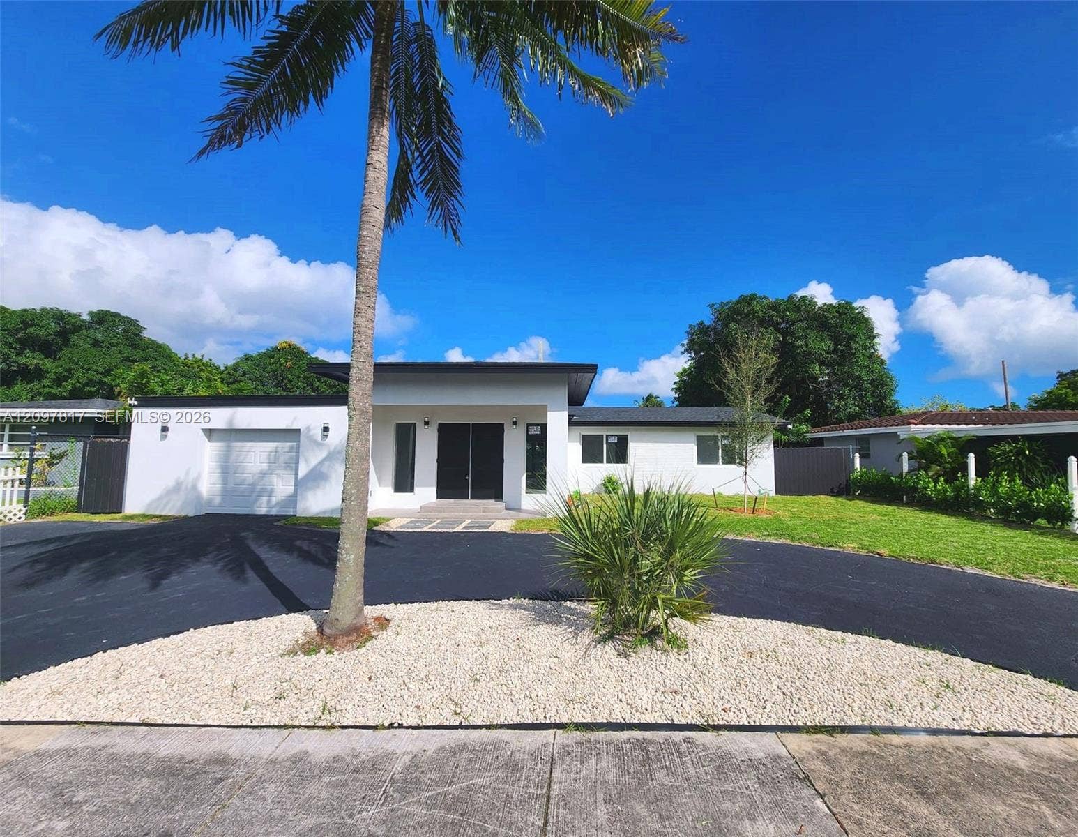Modern single-story exterior featuring a crisp white finish, flat roofline, attached garage, and a wide asphalt driveway with integrated rock landscaping
