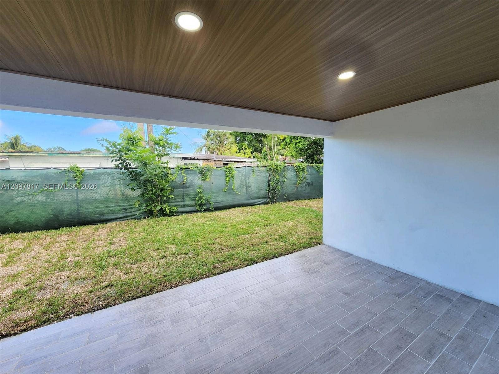 Covered patio featuring wood-finish ceiling paneling, recessed lighting, and tile flooring, opening to a grass lawn