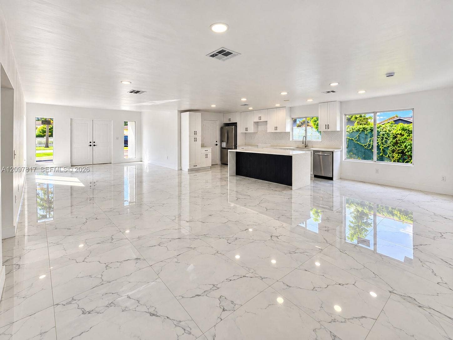 Open-concept interior featuring large-format tile flooring, recessed lighting, white cabinetry, and a kitchen island with a contrasting dark base and white countertop