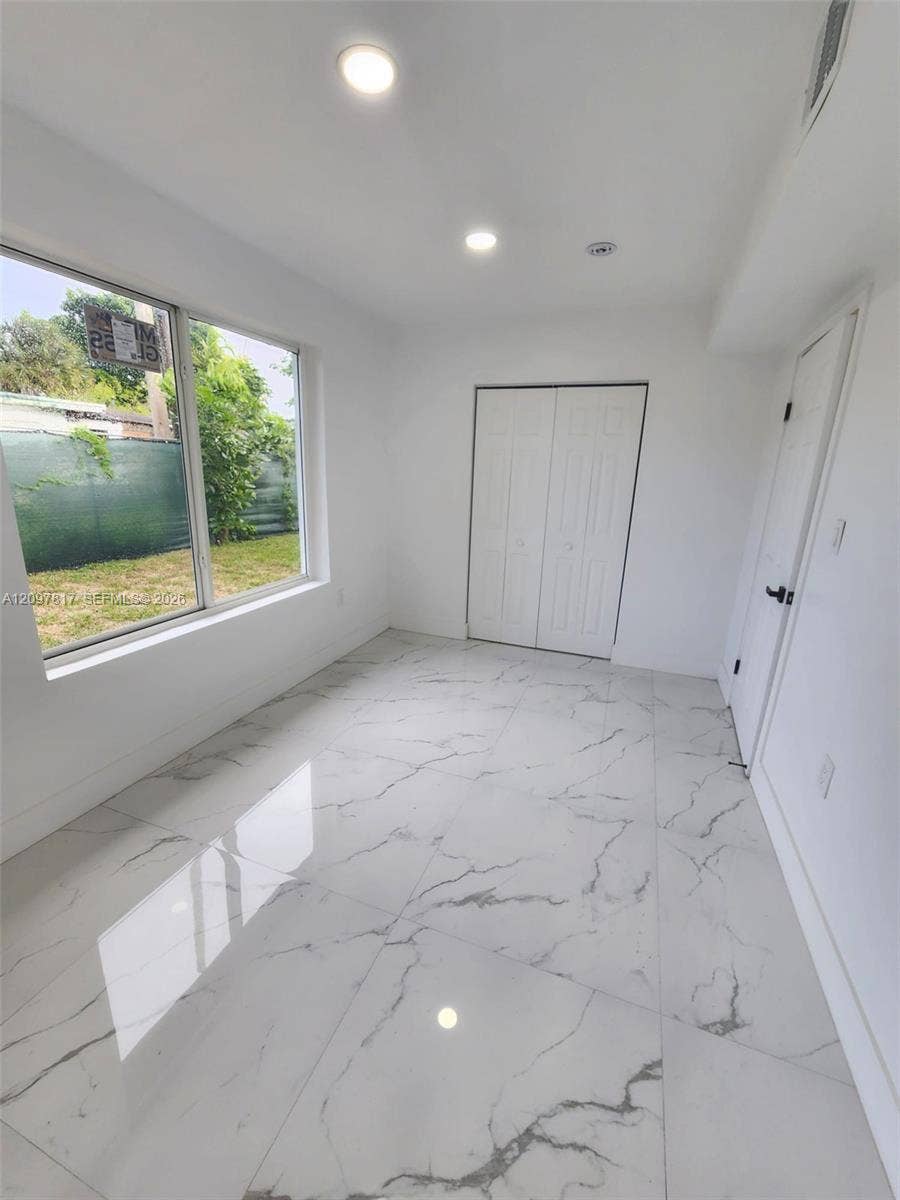 Large-format stone-look tile flooring with veining detail, recessed lighting, and a dual-panel closet door