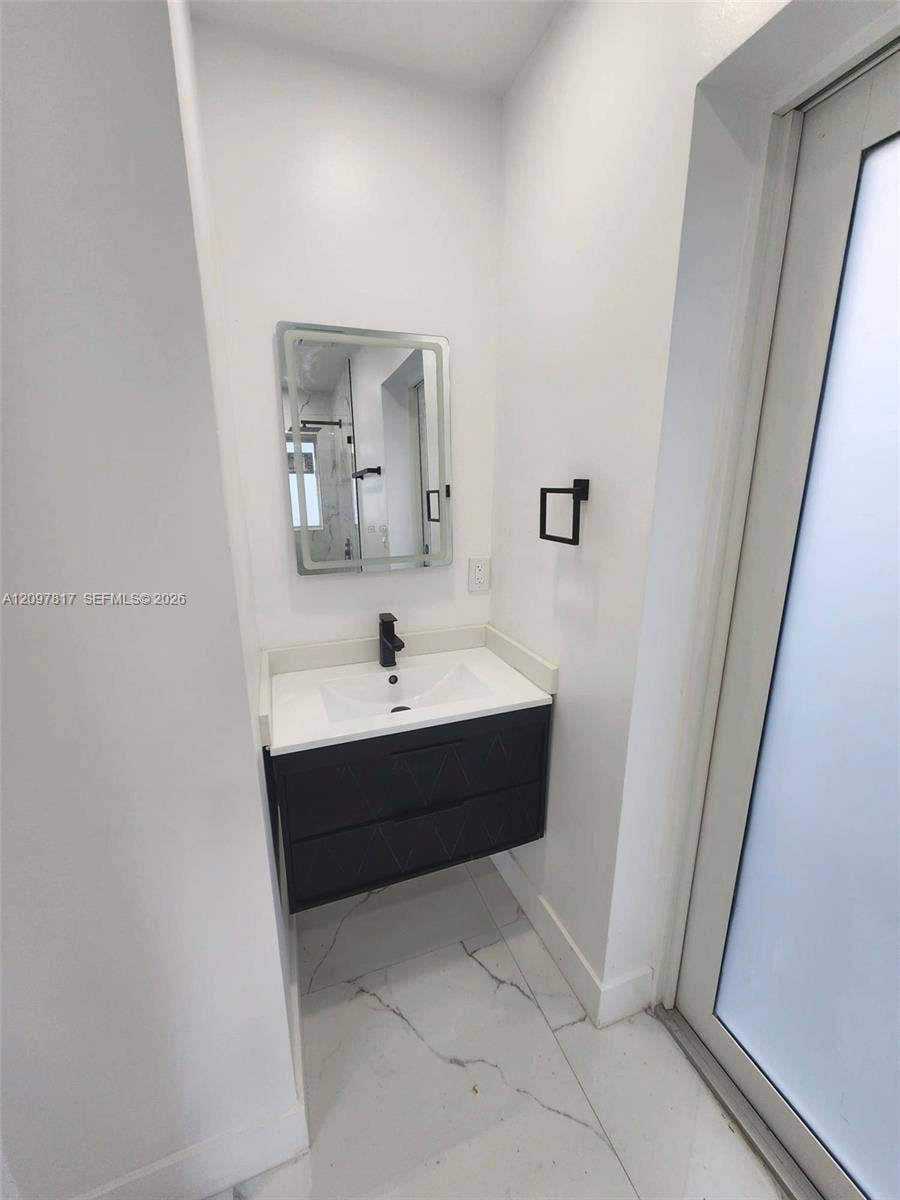 Wall-mounted vanity featuring dual drawers, integrated rectangular sink, stone-finish countertop, matte black faucet, and backlit rectangular mirror, complemented by large-format tile flooring