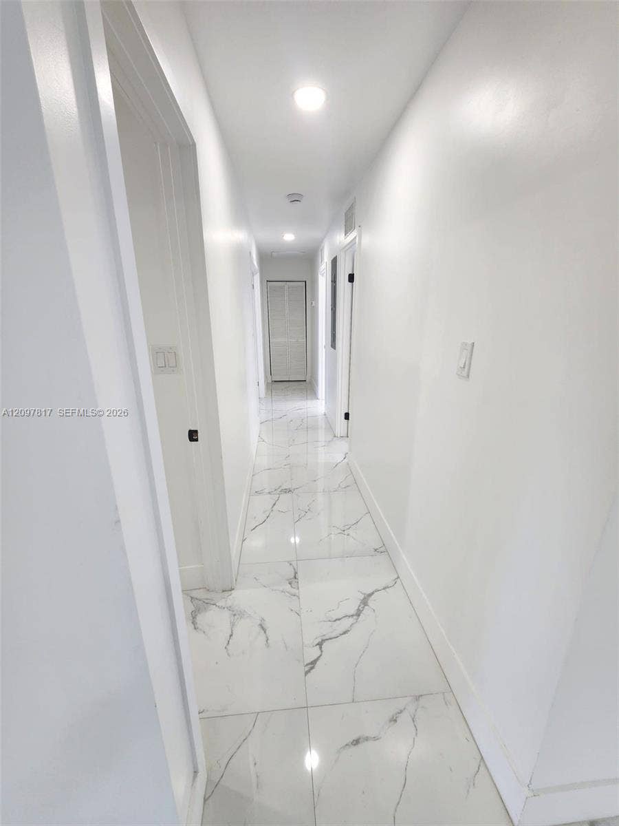 Hallway featuring large-format tile flooring with veined detailing, recessed ceiling lighting, and crisp white wall finishes