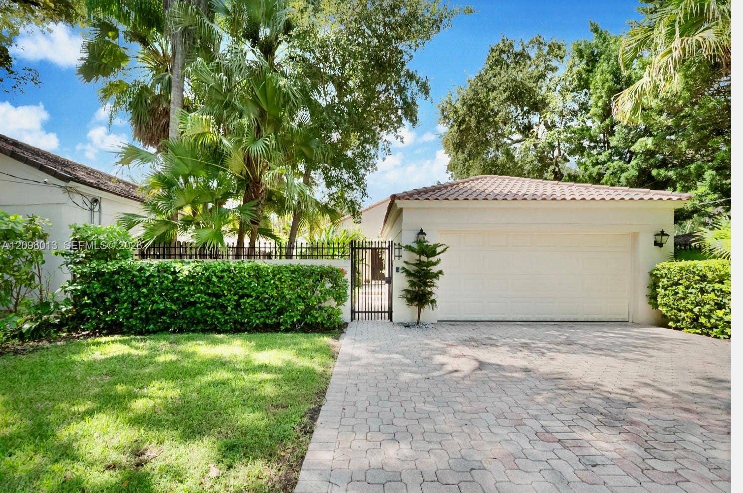 Exterior featuring a paved driveway, metal pedestrian gate, tiled roof, and perimeter wall with integrated greenery