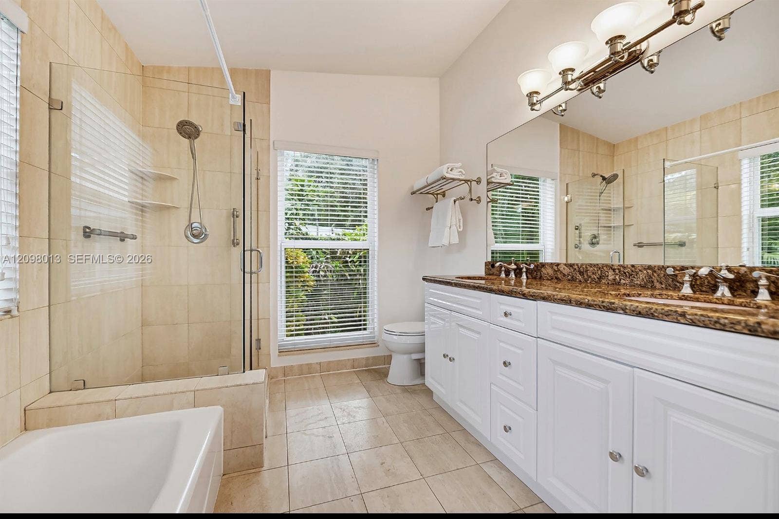 Bathroom featuring a double-sink vanity with stone countertop, walk-in glass-enclosed shower, separate tub tub