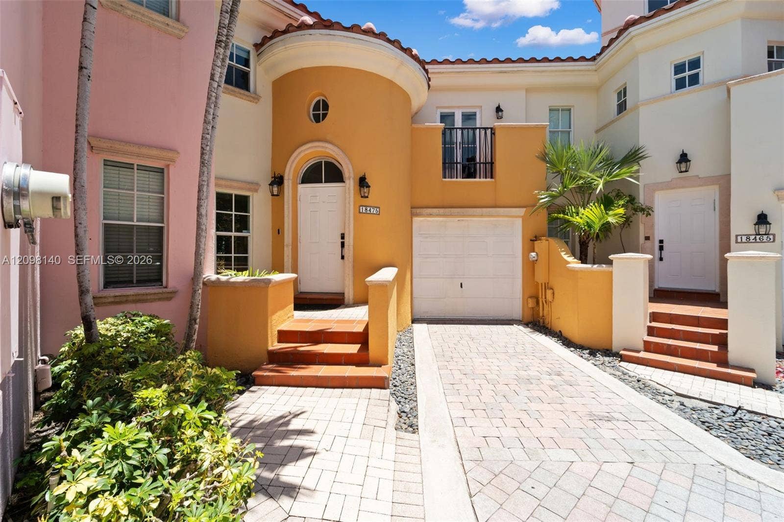 Mediterranean-inspired stucco exterior featuring arched entryway, terracotta-style steps, paver driveway, and a second-story balcony