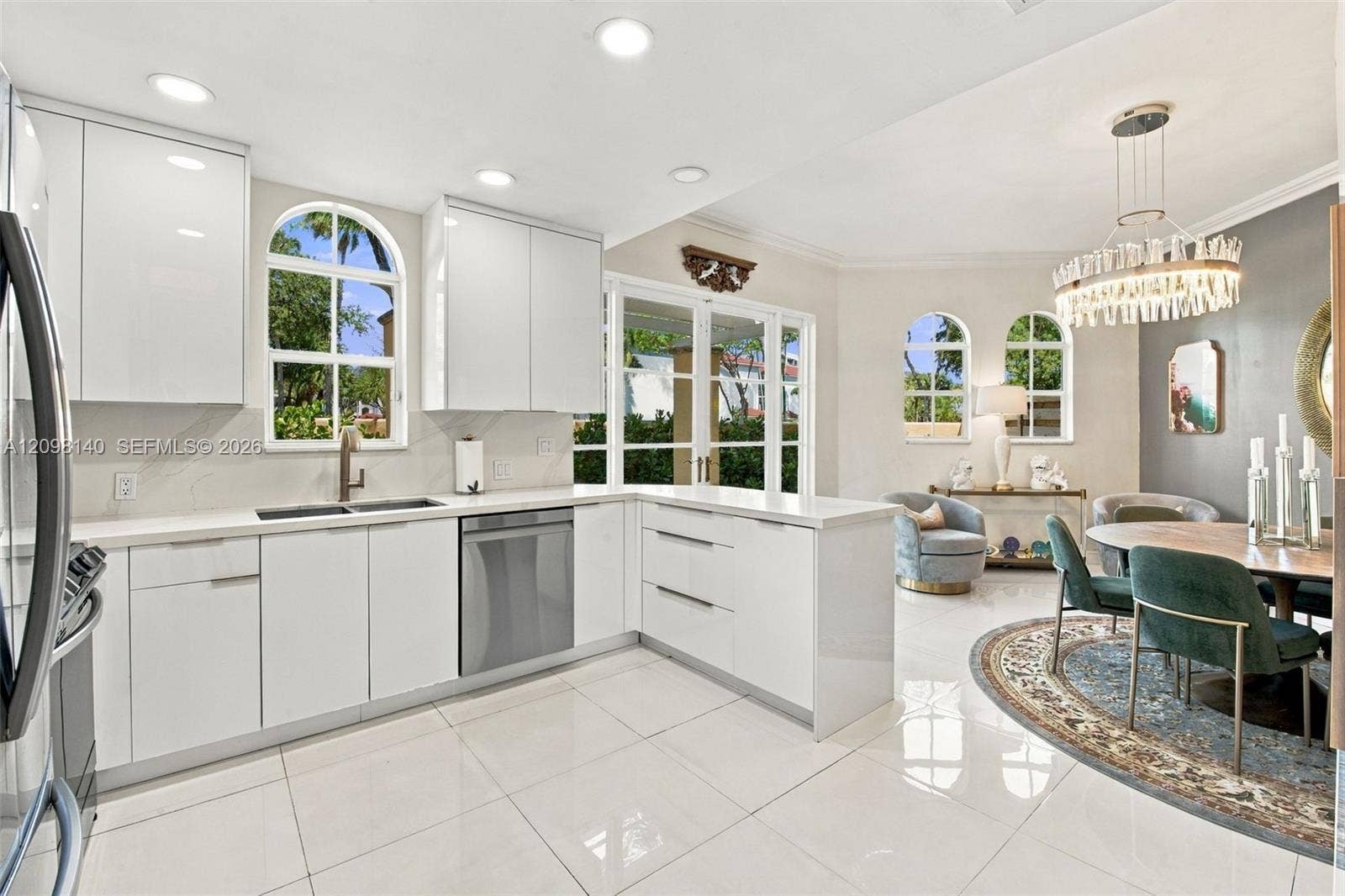 Modern kitchen featuring high-gloss white cabinetry, polished stone countertops, stainless steel appliances, arched windows, and large-format tile flooring