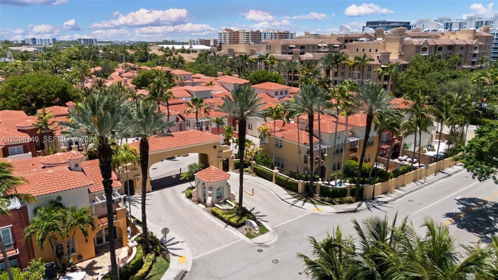 Gated community entrance featuring terracotta tile roofing, stucco exterior finishes, a dedicated guardhouse, and mature landscaping