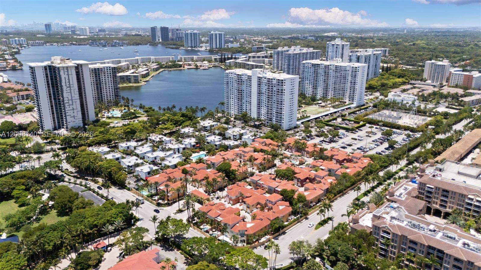 Aerial perspective of a low-rise residential community featuring terra-cotta tile roofing, mature landscaping, proximity to local water bodies, and expansive urban infrastructure