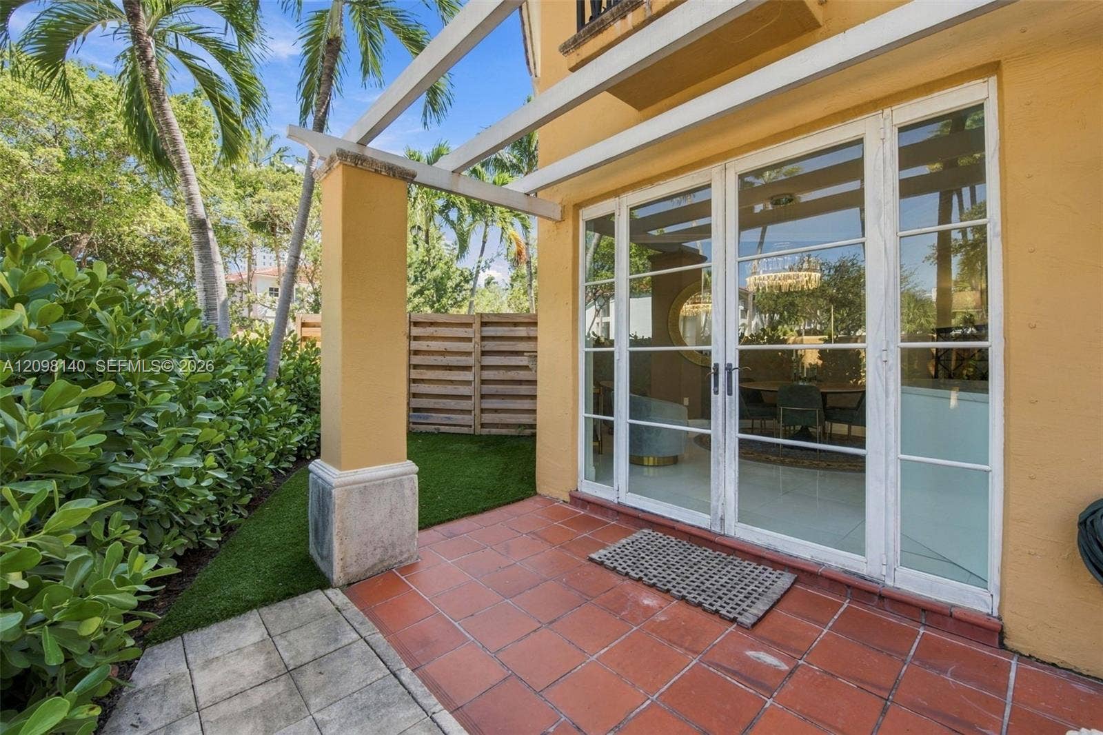 Rear patio featuring terracotta tile flooring, a white structural pergola, synthetic turf, and full-height glass French doors with white mullions