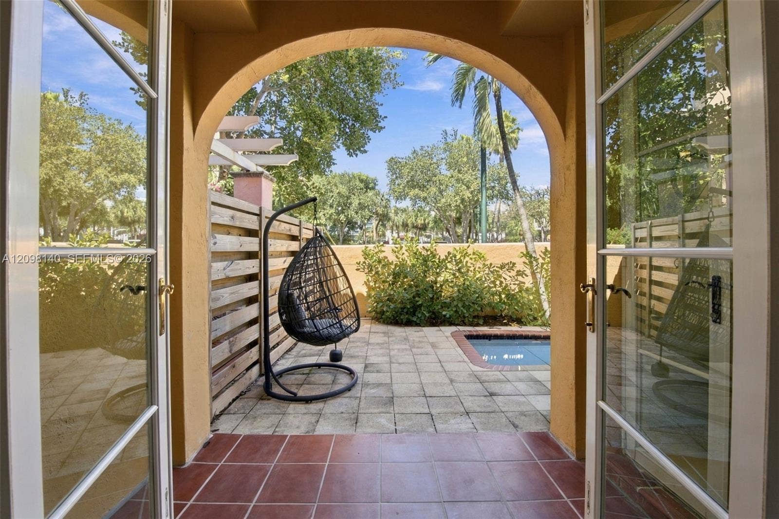 Arched double glass doors opening to a tiled patio featuring a pool and horizontal wood privacy fencing