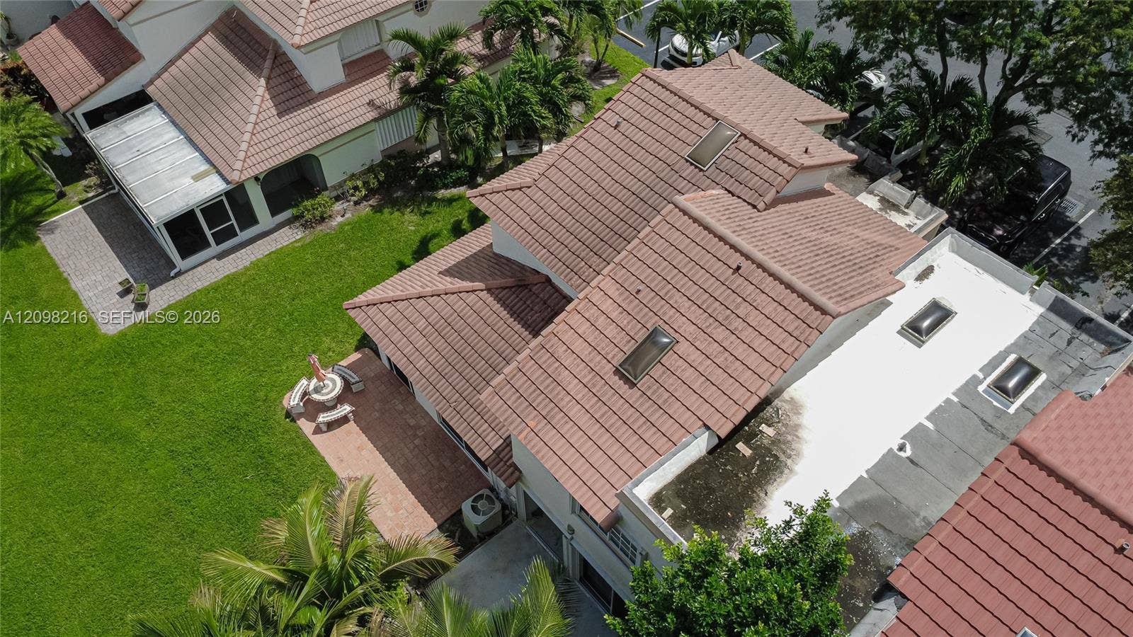 Aerial view of the home and its tile roof, surrounded by mature landscaping and green space.