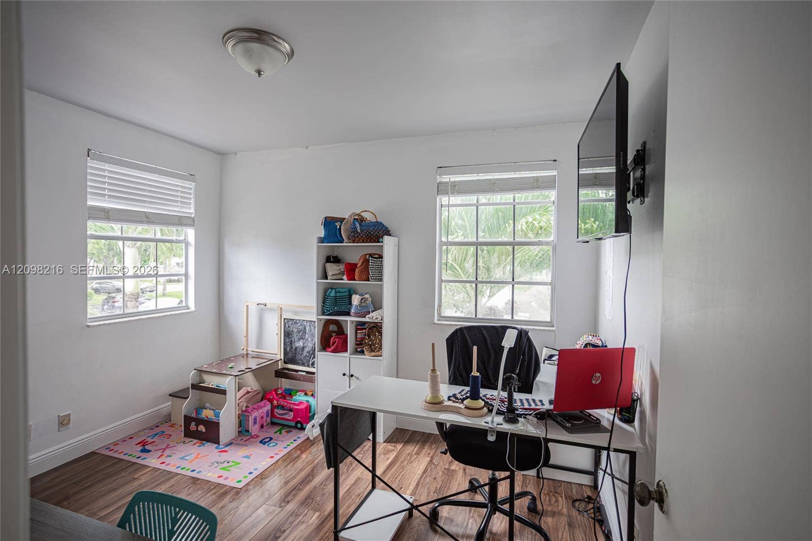 Bright, flexible room set up as a home office, with two windows and wood style floors.
