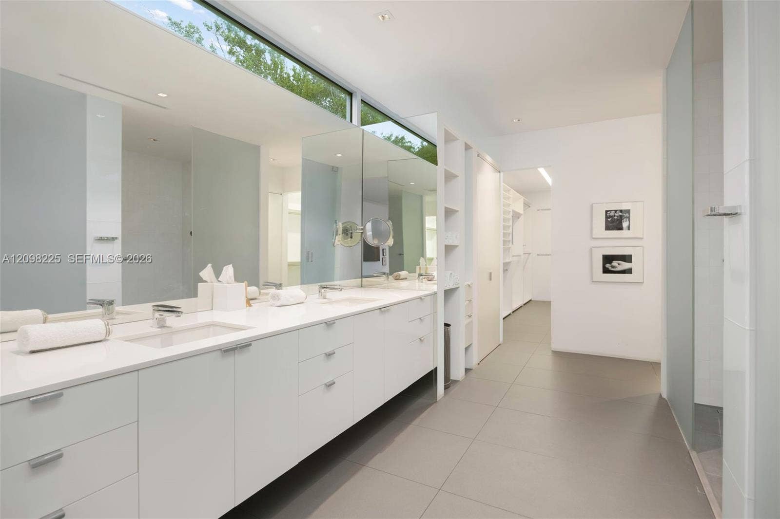 Dual-sink vanity with clean-lined cabinetry, stone-finish countertops, expansive horizontal mirror, transom window, and large-format tile flooring