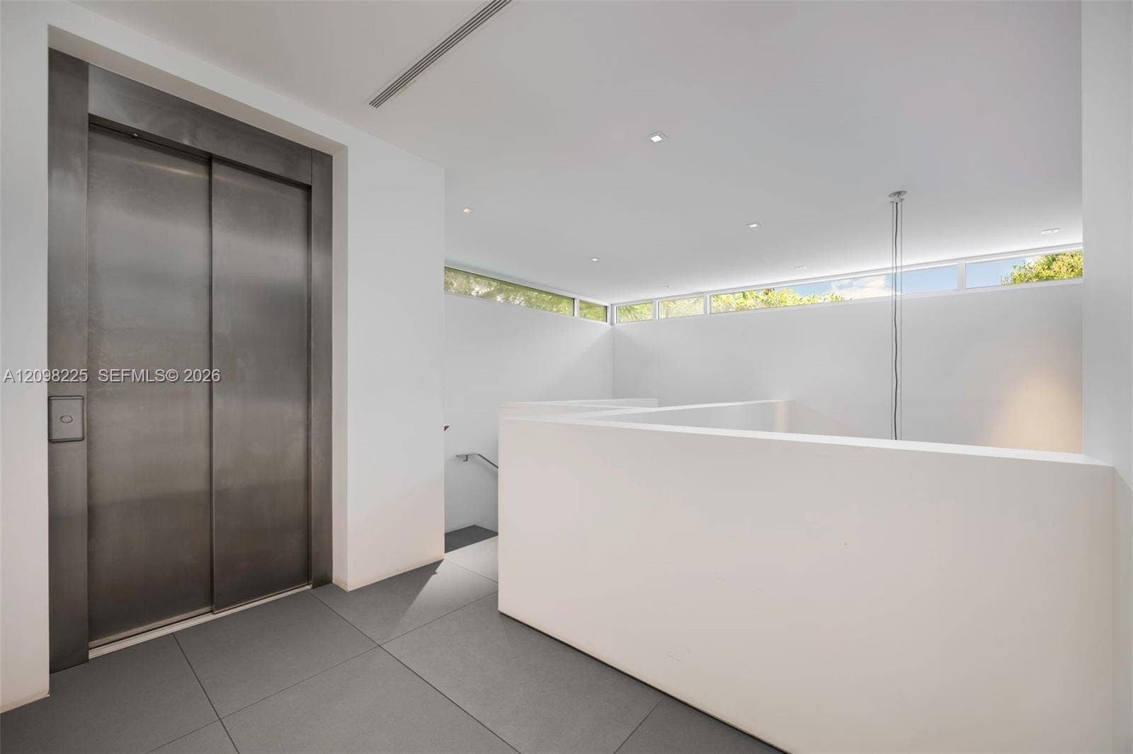 Stainless steel elevator, minimalist white walls, clerestory windows, recessed ceiling lighting, and large-format tile flooring