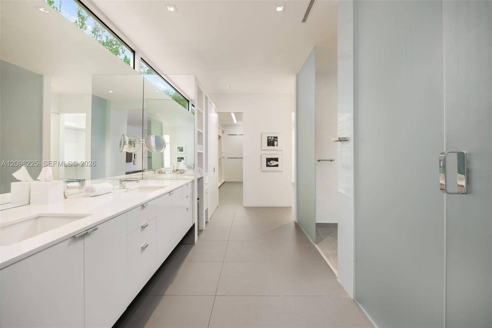 Dual vanity with white cabinetry, solid-surface countertop, full-width mirror, transom window, and tile flooring