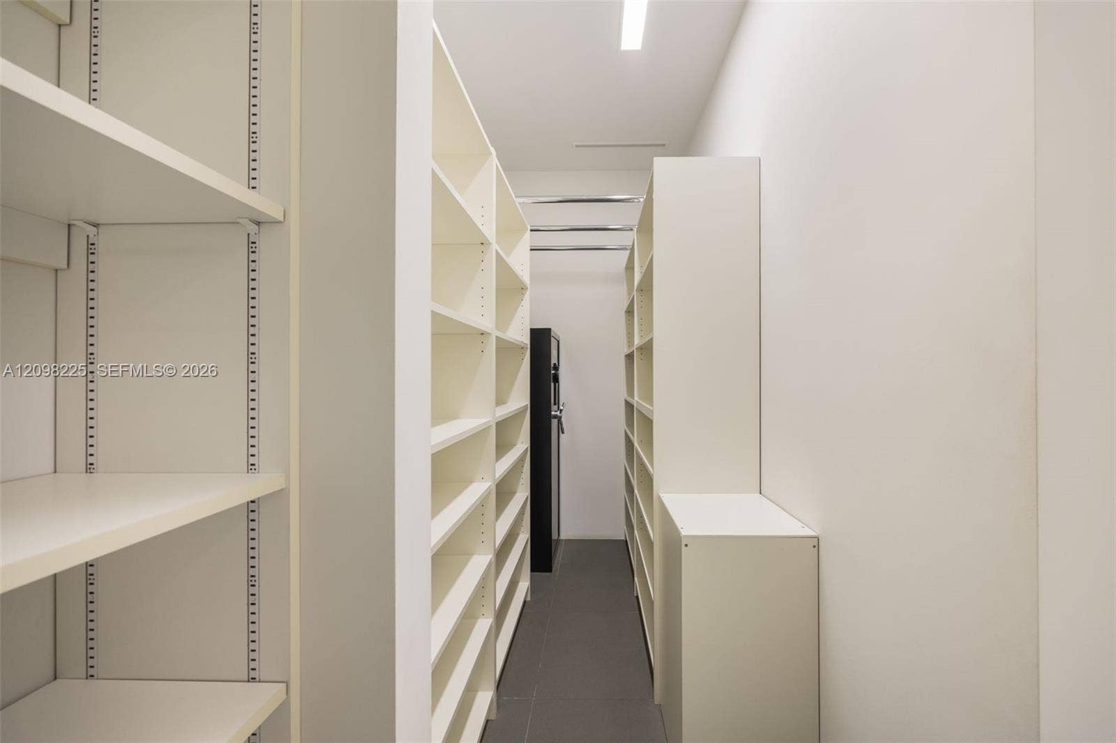 Floor-to-ceiling built-in white shelving, adjustable shelving hardware, overhead recessed lighting, and large-format tile flooring