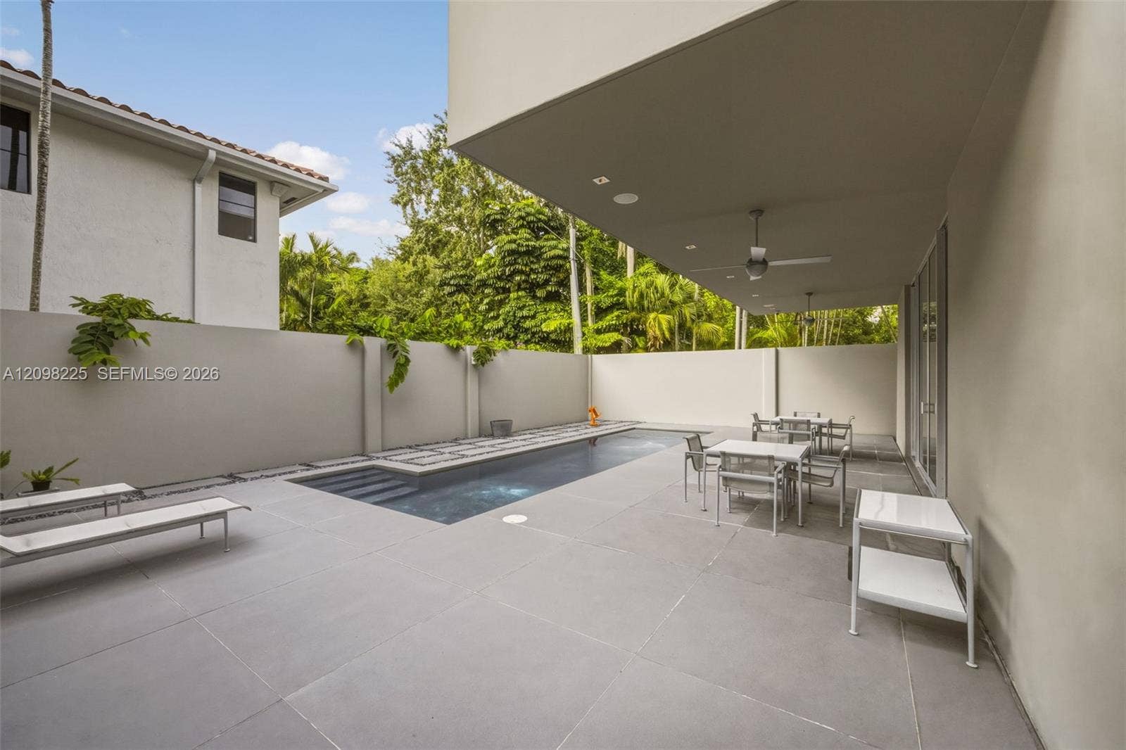 Covered patio featuring recessed ceiling lighting, ceiling fans, large-format stone pavers, a rectangular swimming pool, and a perimeter privacy wall