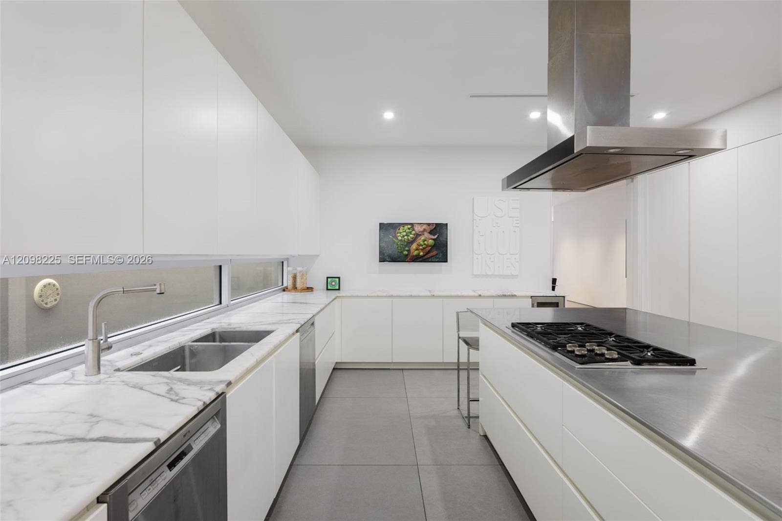 Contemporary kitchen featuring flat-panel cabinetry, stone countertops, stainless steel island cooktop with hood, and large-format tile flooring