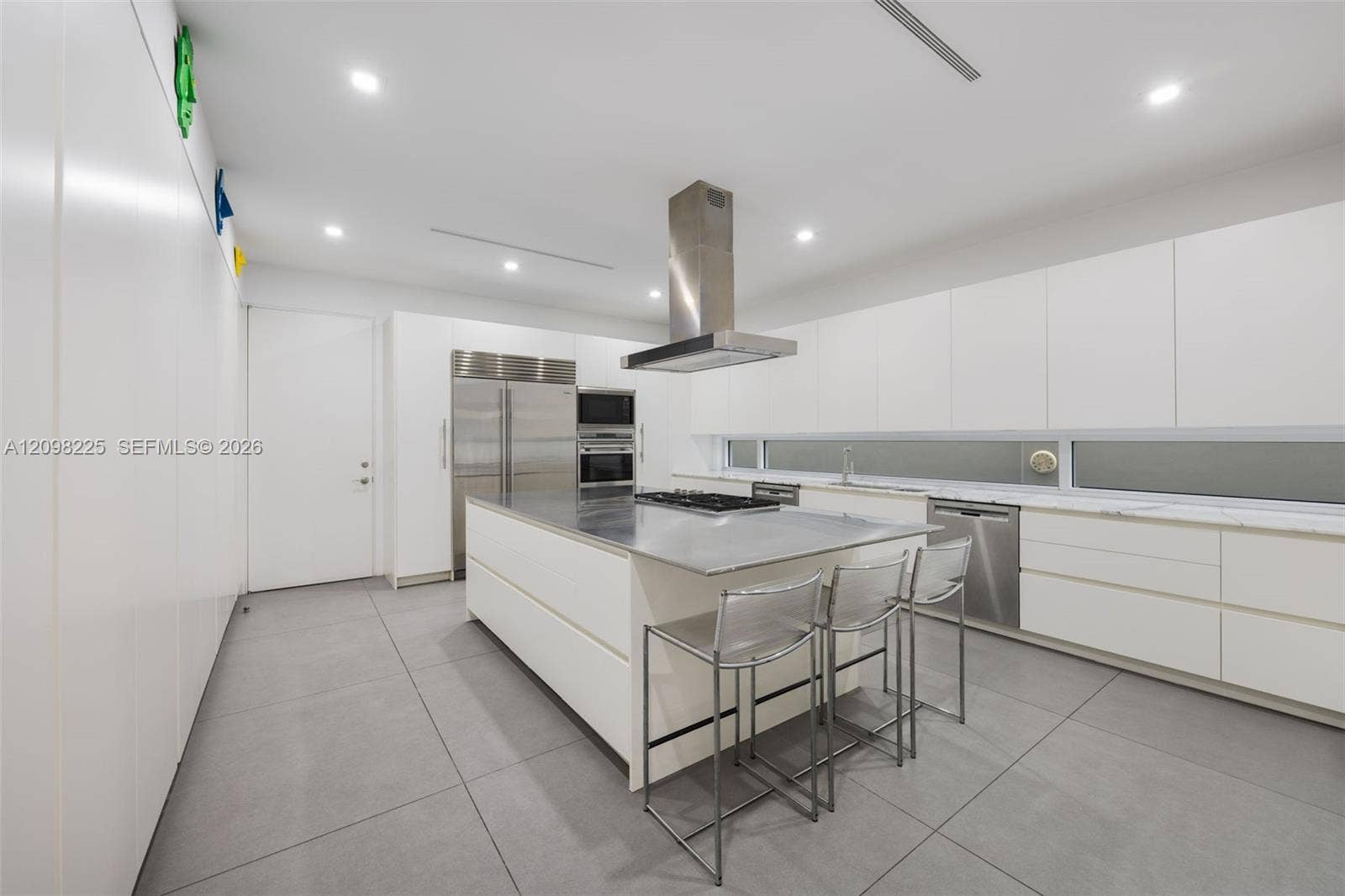 Contemporary kitchen featuring flat-panel cabinetry, a central island with a stainless steel countertop, professional-grade stainless steel appliances, a linear horizontal window, and large-format porcelain tile flooring