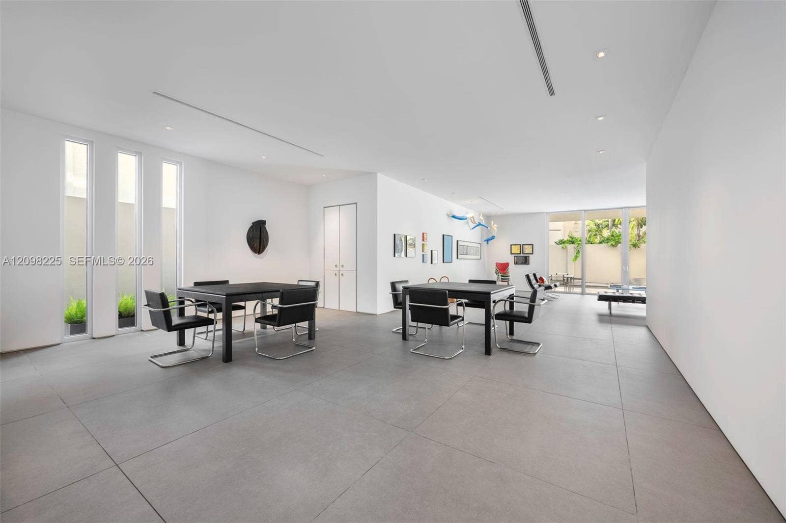 Expansive open-concept room featuring large-format tile flooring, recessed linear lighting, floor-to-ceiling windows, and glass sliding doors