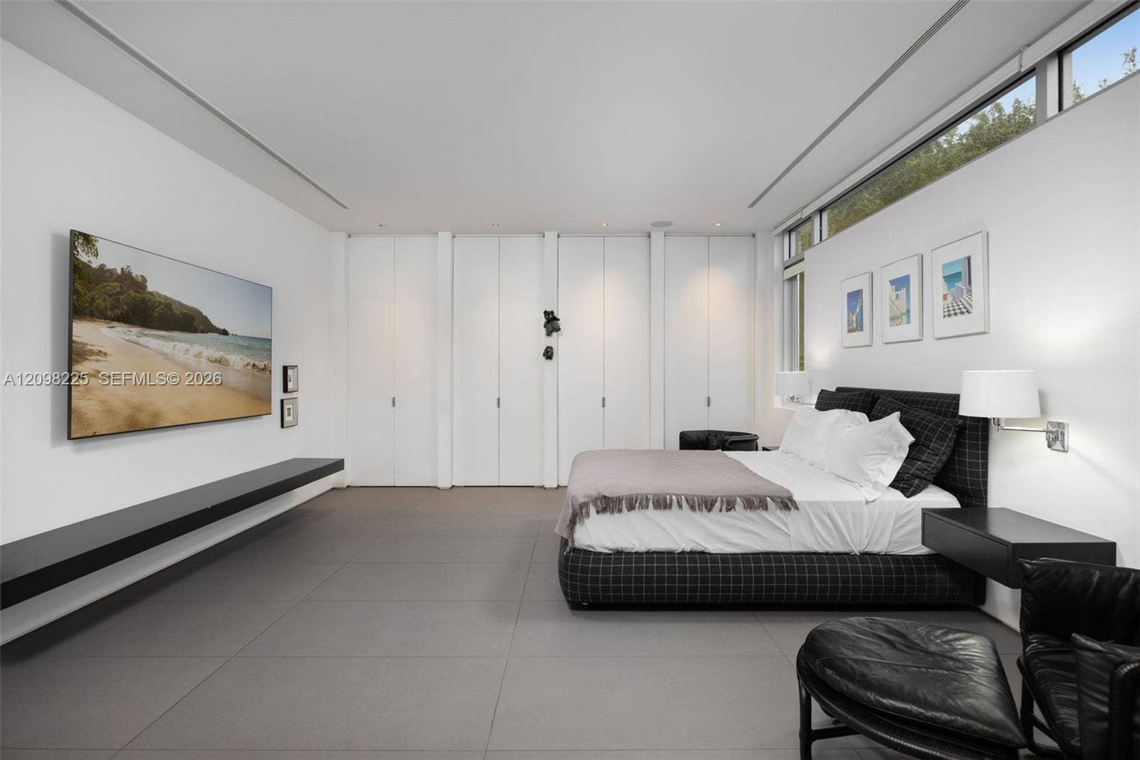 Large-format tile flooring, expansive wall of floor-to-ceiling built-in cabinetry, high-set horizontal windows, recessed ceiling lighting, and a wall-mounted floating shelf