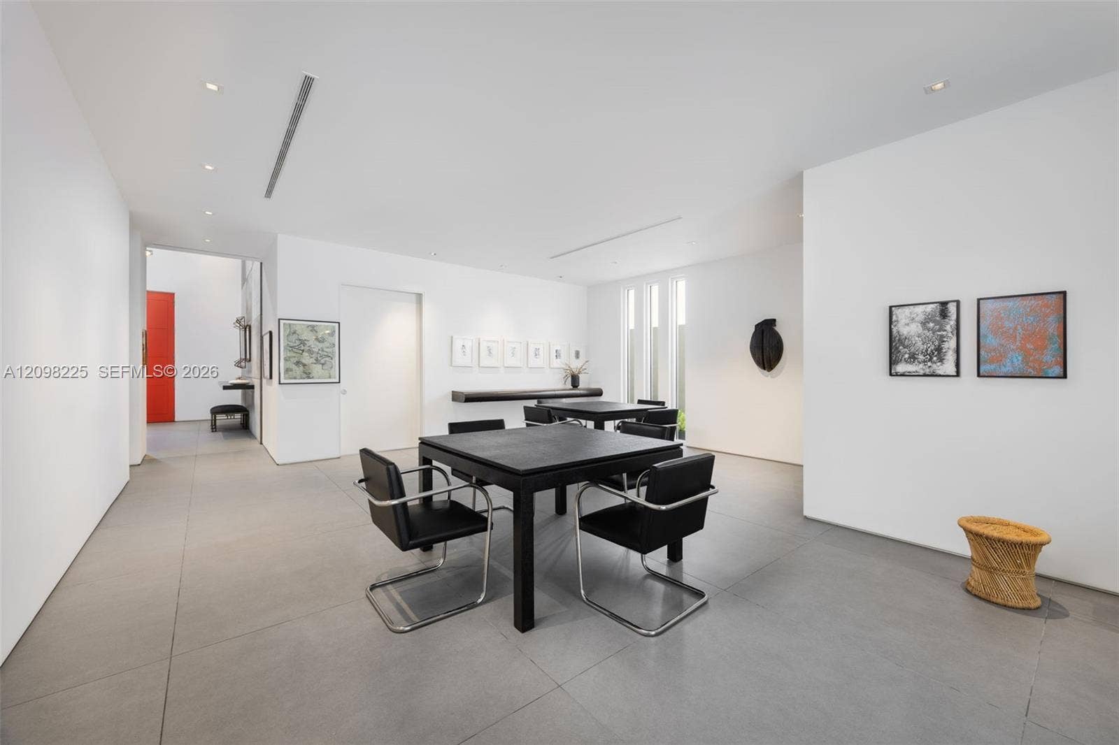 Open-concept interior featuring large-format tile flooring, smooth white walls, recessed ceiling lighting, and a built-in linear shelving unit
