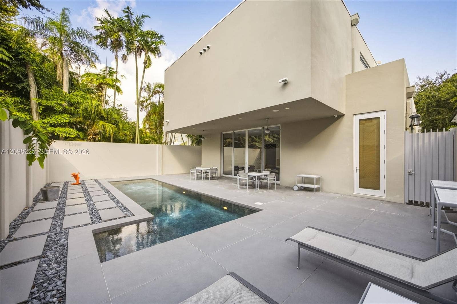 Modern stucco exterior featuring a swimming pool, concrete paver decking, decorative stone border, and privacy perimeter wall