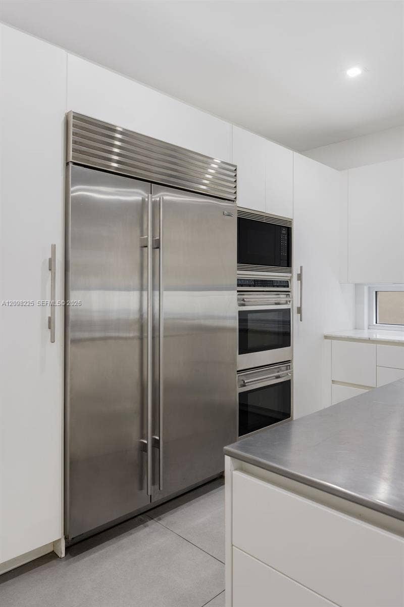 Kitchen featuring flat-panel white cabinetry, stainless steel built-in double-door refrigerator, integrated stainless steel double oven, stainless steel microwave, and metal countertop