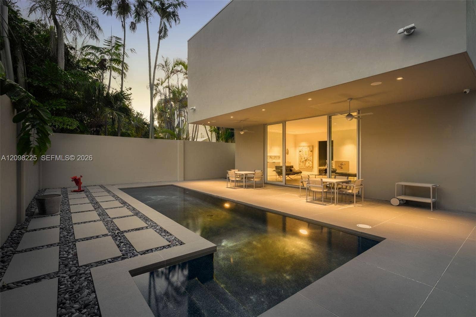 Modern architectural exterior featuring a swimming pool, large format tile patio, stone-bordered concrete pavers, and full-height sliding glass doors