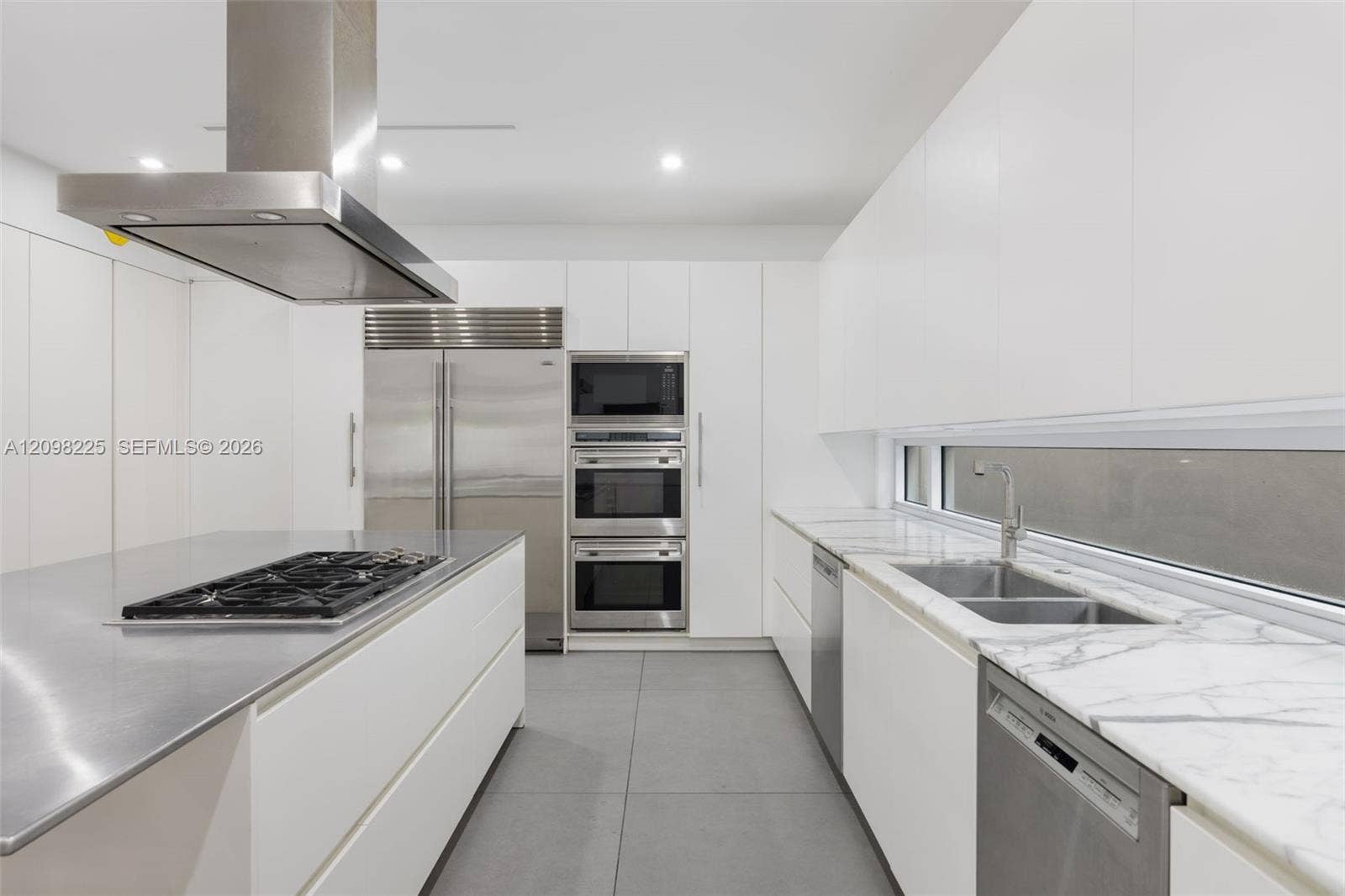 Contemporary kitchen featuring flat-panel cabinetry, stainless steel island countertop with integrated cooktop, stone-surface perimeter countertops, stainless steel wall ovens, and recessed ceiling lighting