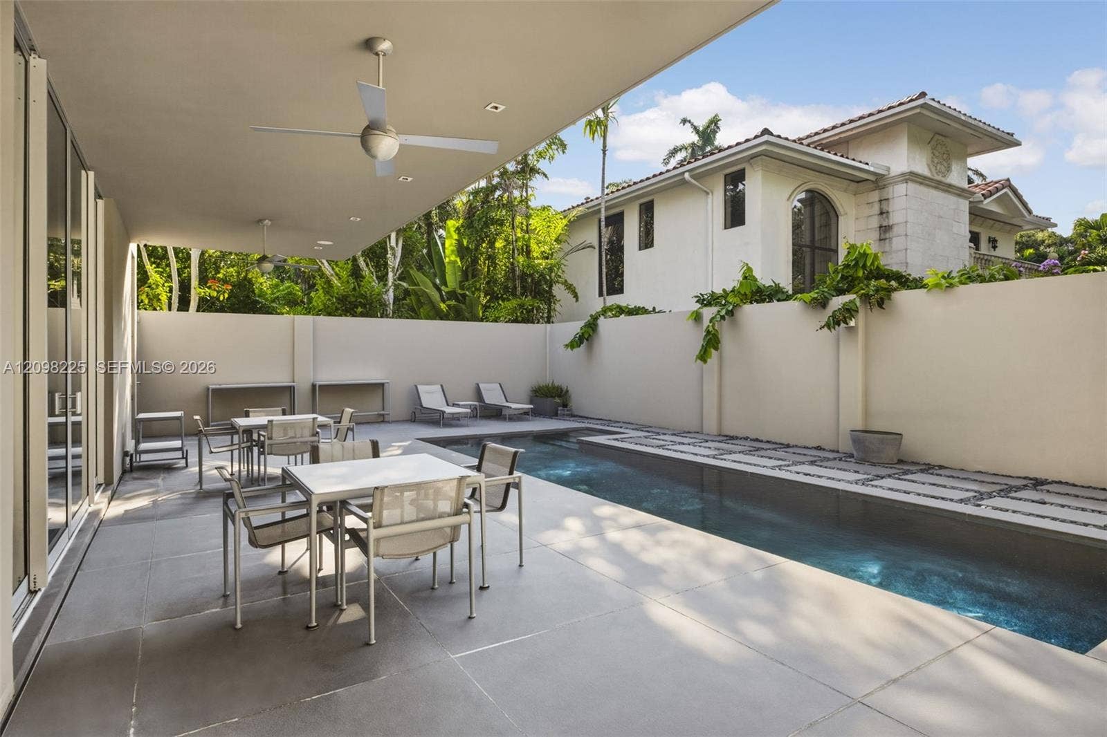 Covered outdoor patio featuring large-format concrete tile flooring and recessed ceiling fans, complemented by a private lap pool with stone pavers