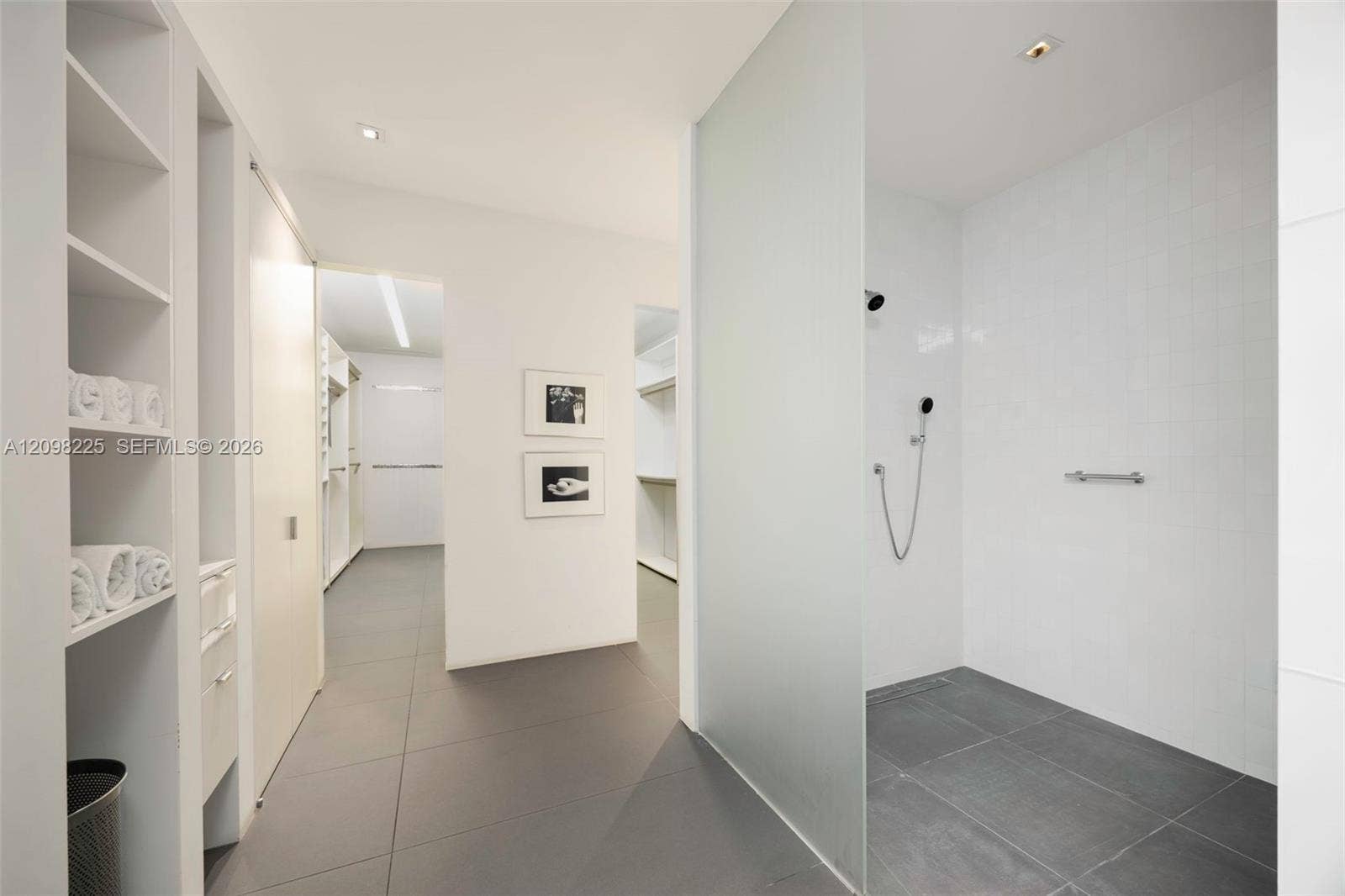 Walk-in shower featuring a frosted glass partition, matte black wall-mounted shower head, and large-format tile flooring, accompanied by built-in white shelving and cabinetry