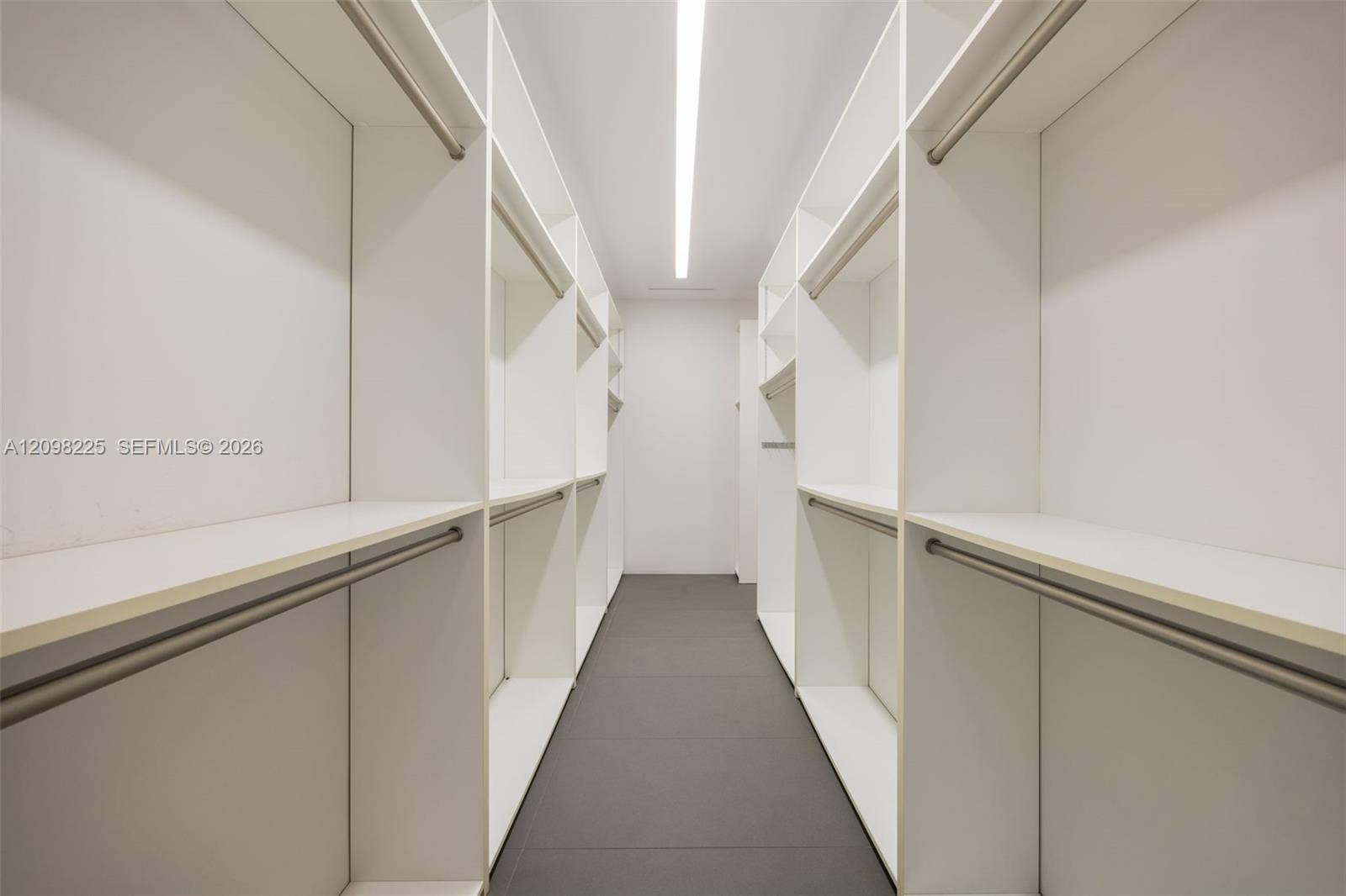 Walk-in closet featuring white built-in shelving, integrated hanging rods, flush-mount linear ceiling lighting, and tile flooring