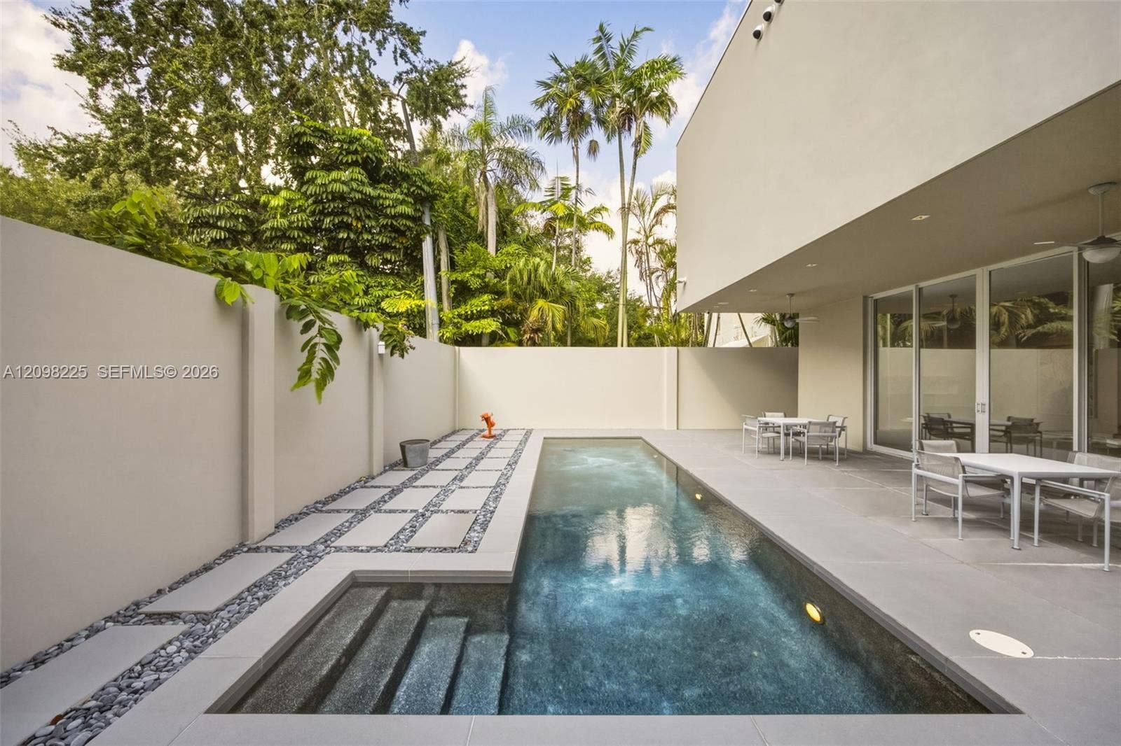 Rectangular swimming pool featuring integrated steps, surrounded by large-format concrete patio tiling, decorative stone-accented pathways, and solid perimeter wall fencing