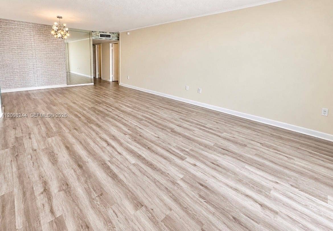 2851 NE 183rd Street, #2110E, Aventura, Aventura, FL 33160 Expansive interior space featuring wood-finish flooring, a textured accent wall, mirrored wall paneling, and a multi-bulb decorative chandelier